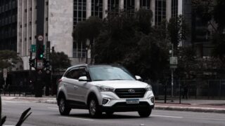 White SUV traveling on city road against towering buildings.