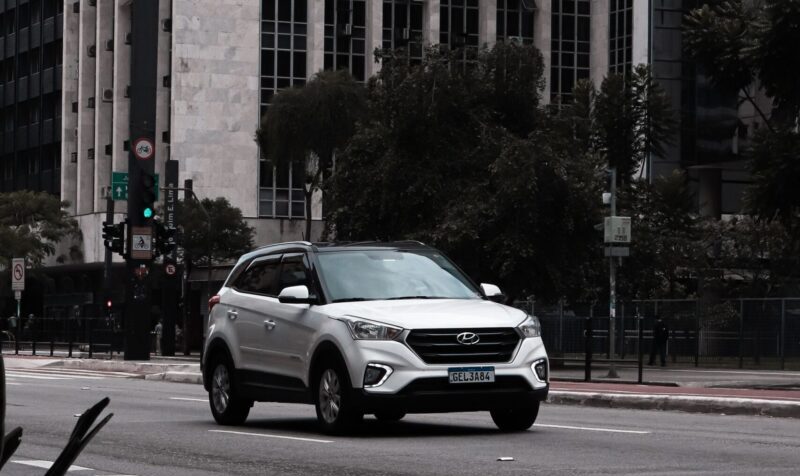 White SUV traveling on city road against towering buildings.